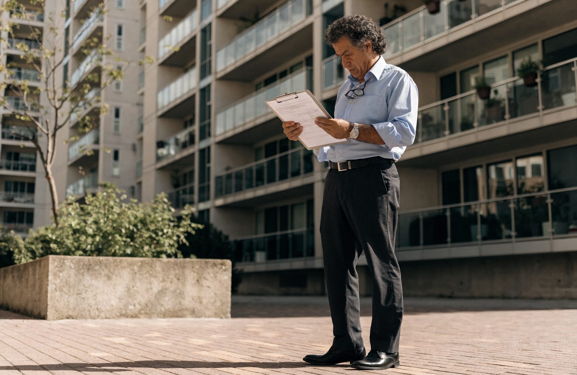 A condo-association board member reviewing building inspection documents in front of a modern residential condominium